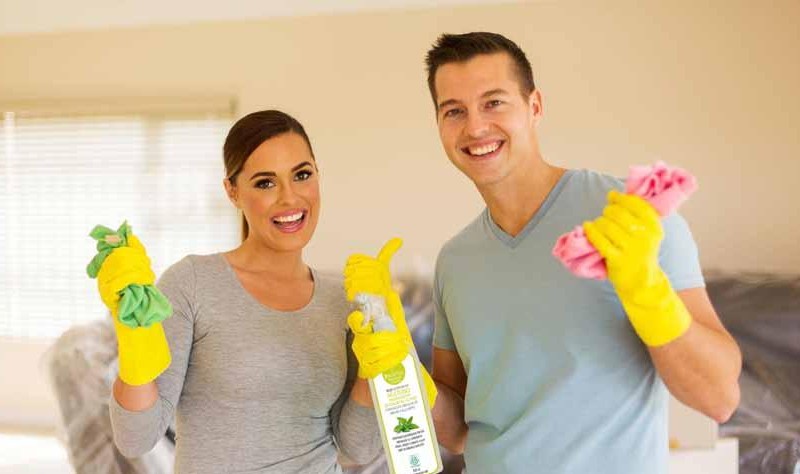 a couple is smiling and holding spray bottles and wipes in their hands