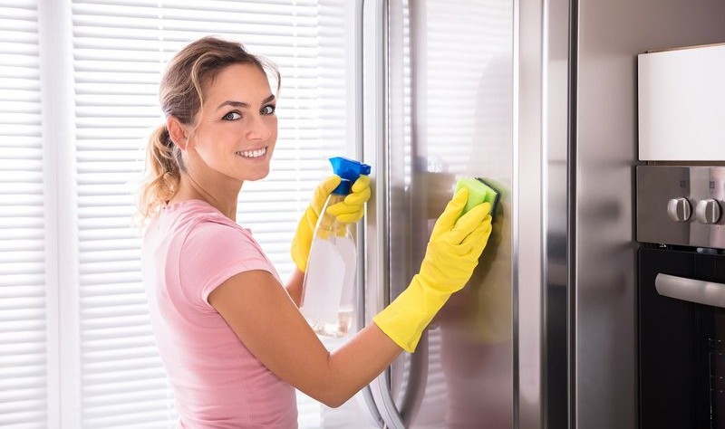 a beautiful young woman with yellow gloves wiping a refrigerator with a sponge