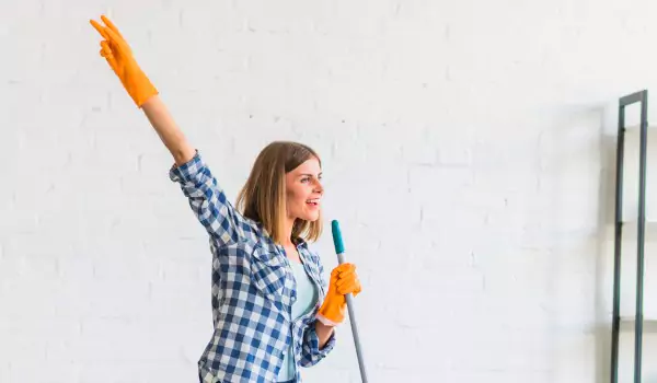 Woman enjoying while cleaning her house holding a wiper as a mic